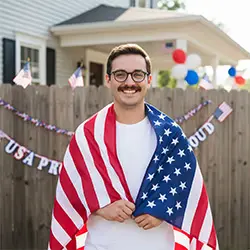Smiling man wrapped in the American flag celebrating USA Independence Day at Dr. Jyoti Dharmdas Homeo Clinic, Bhopal – trusted for holistic care by the best homeopathy doctor in Bhopal, Dr. Renu Rajput Barigal.
